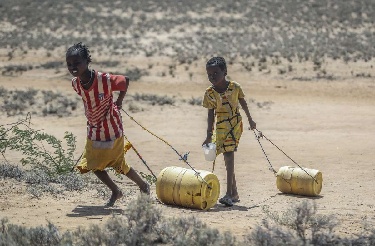 Zwei junge Mädchen ziehen Wasserbehälter auf dem Rückweg zu ihren Hütten im kenianischen  osionUmweltzerstörung.