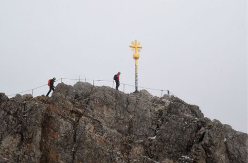 Bergsteiger gehen zum Gipfelkreuz des Zugspitzgipfel bei Wolken und leichtem Schneetreiben. Bei Temperaturen um den Gefrierpunkt hat man vom Gipfel aus kaum Sicht ins Tal. Foto: Felix Hörhager/dpa