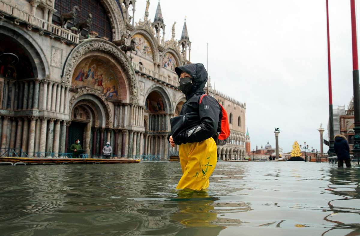 Eine Passantin bahnt sich ihren Weg durch den überfluteten Markusplatz. Starke Regenfälle und steigende Pegel haben im italienischen Venedig Teile der Stadt überflutet.