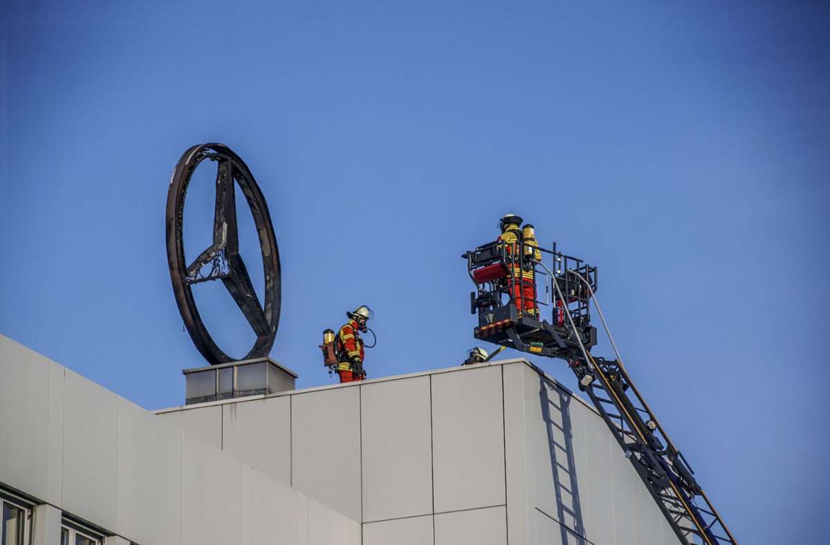 Feuerwehrleute stehen neben einem verbrannten Mercedes-Stern auf dem Dach eines Firmengebäudes. Foto: dpa/Dettenmeyer