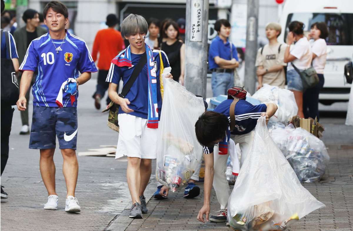 Fans der japanischen Nationalmannschaft sammeln Müll in Tokio ein, nachdem sie beim Public Viewing das Spiel zwischen Japan und Belgien  gesehen haben Foto: dpa/–