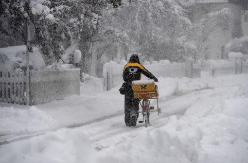 Ein Postbote schiebt sein Fahrrad durch den hohen Schnee. Foto: dpa/Angelika Warmuth
