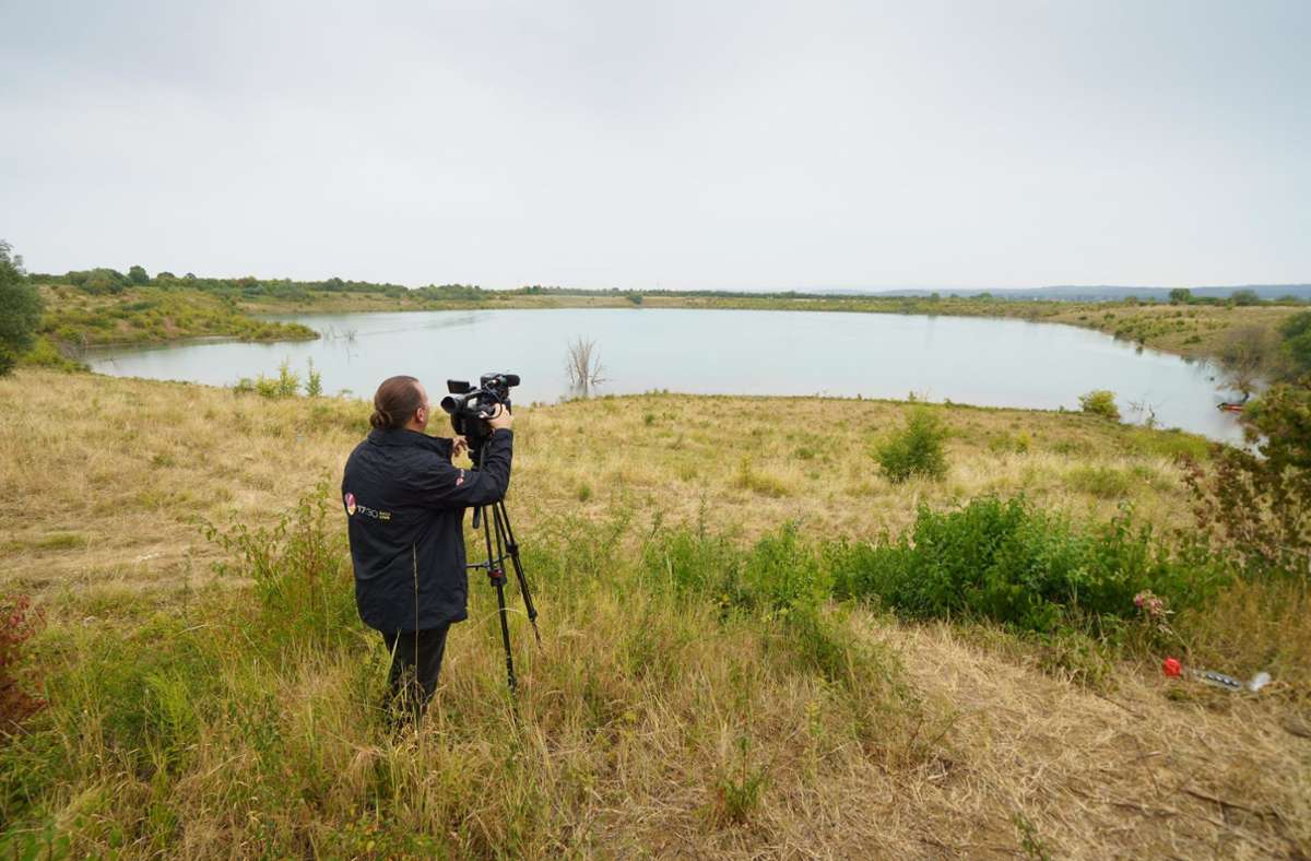 Ein Kameramann filmt am Ufer des Teufelsees im hessischen Wetteraukreis, in dem die Leiche der 14-jährigen Ayleen gefunden wurde. (Archivbild) Foto: dpa/Frank Rumpenhorst