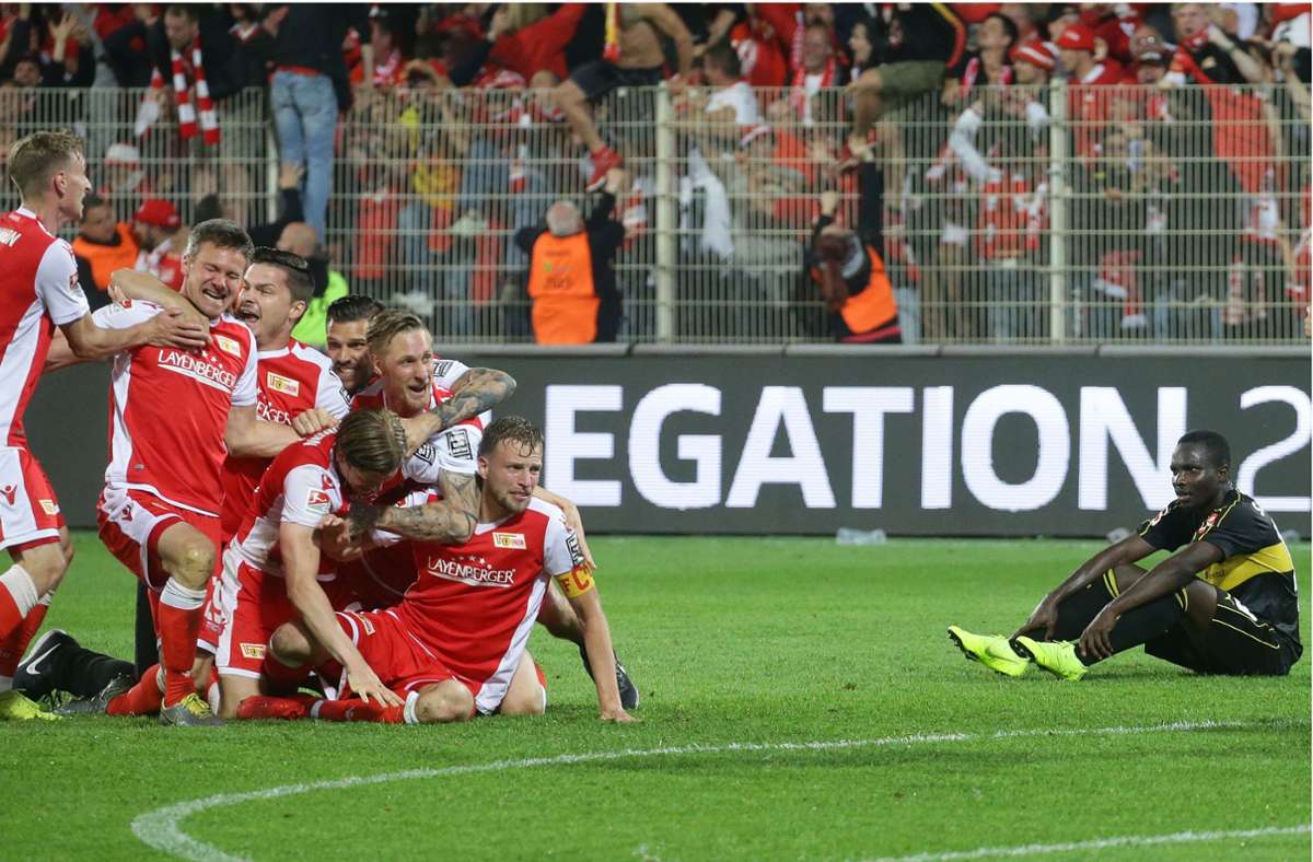 Die Union-Spieler feiern 2019 ausgelassen –  Chadrac Akolo (re.) und der VfB Stuttgart sind am Boden. Dass sich der Zweitligist in den Relegationsspielen durchsetzt, kommt selten vor.