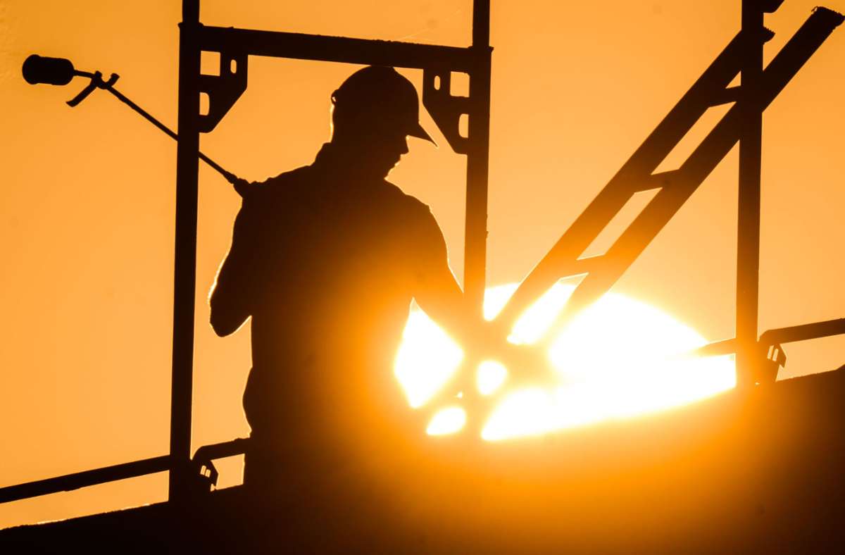 Ein Bauarbeiter steht mit einem Gasbrenner beim Bau eines Mehrfamilienhauses, als am Horizont die Sonne aufgeht. Foto: dpa/Julian Stratenschulte