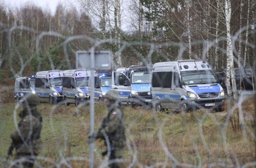 Polnische Grenzschutzbeamte stehen hinter einem Stacheldrahtzaun Wache, während sich an der weißrussisch-polnischen Grenze Migranten versammelt haben. Foto: dpa/Leonid Shcheglov