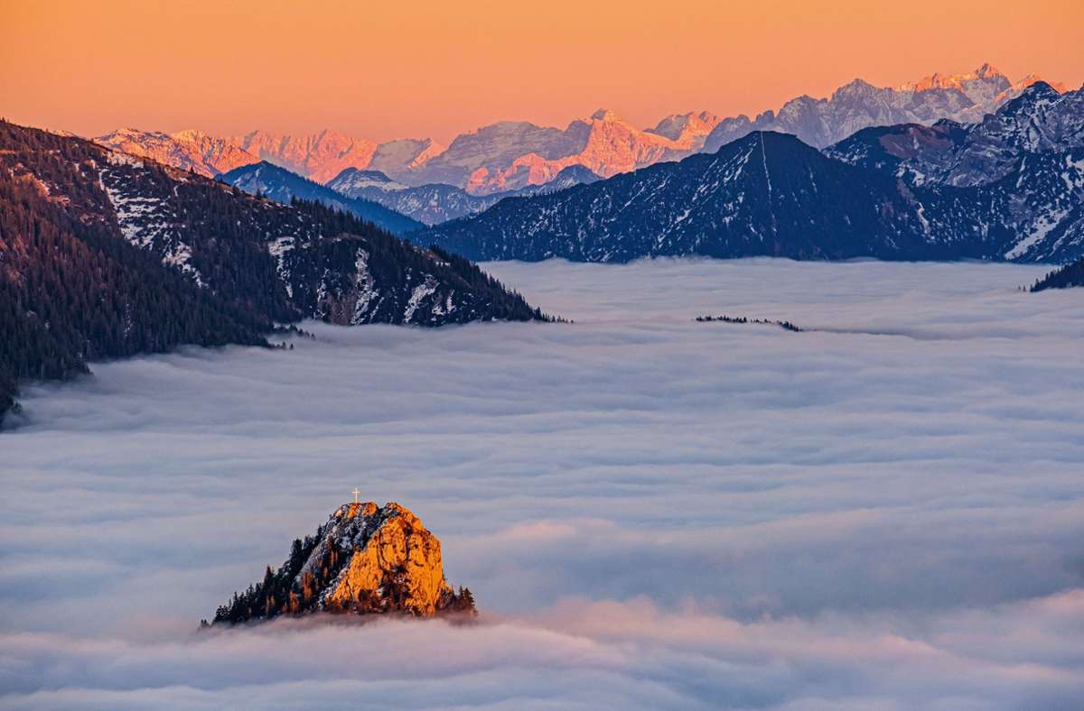 An einem  Novemberabend umhüllt der Hochnebel den Leonhardstein in den bayerischen Voralpen. Im Hintergrund thronen die Gipfel des Wilden Kaisers und der Loferer Steinberge.
