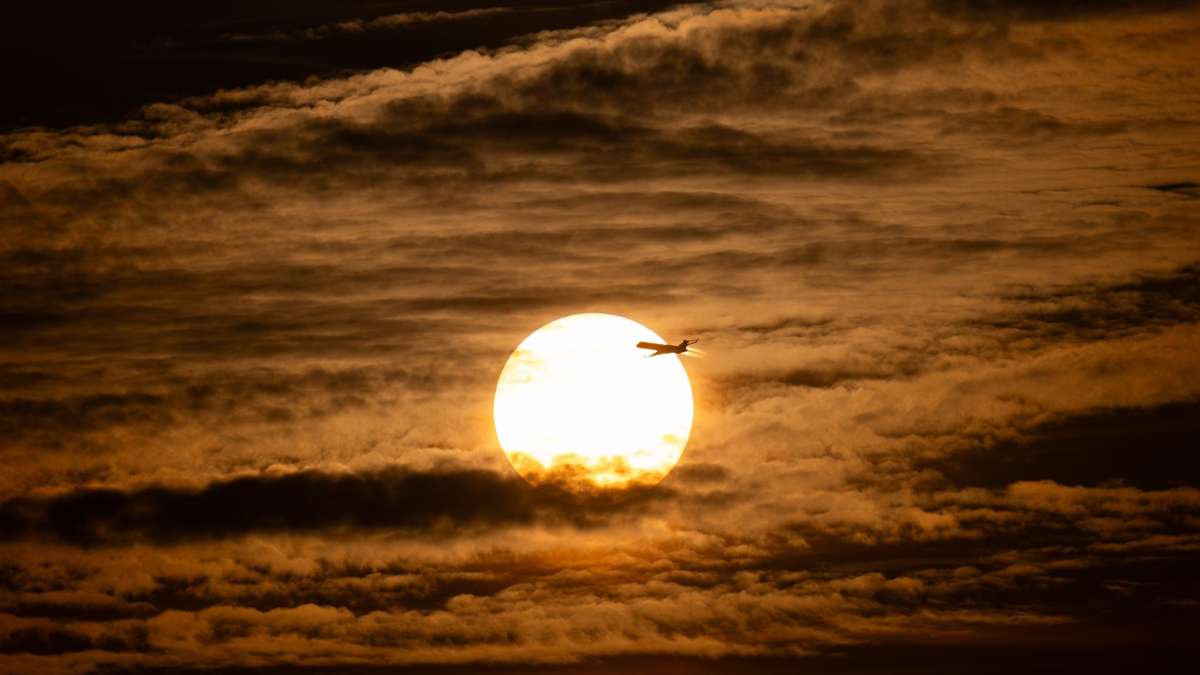 Der Tag geht zu Ende: Ein Flugzeug fliegt vor der untergehenden Sonne über Frankfurt am Main.