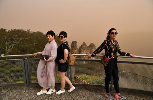 Drei Touristinnen stehen auf einem Aussichtspunkt in Sydney, während Rauchschleier die Landschaft einhüllen. Die Waldbrände haben zu einem Rückgang der  Gästezahlen geführt. Foto: dpa